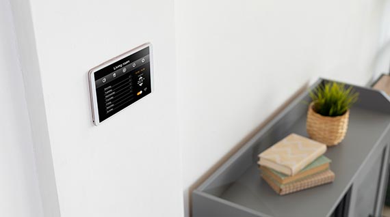 A wall mounted smart home controller with a book on the shelf.